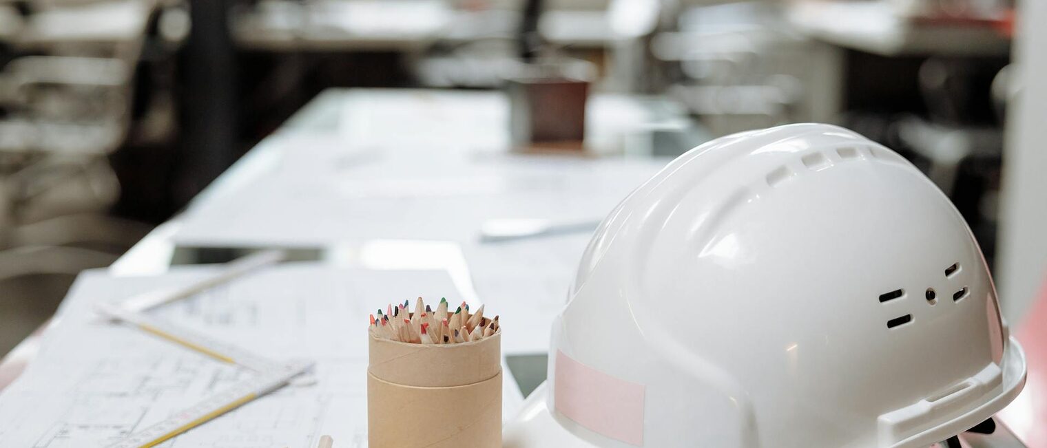 Weißer Schutzhelm auf einem weißem Tisch mit Dokumenten und Bundstiften